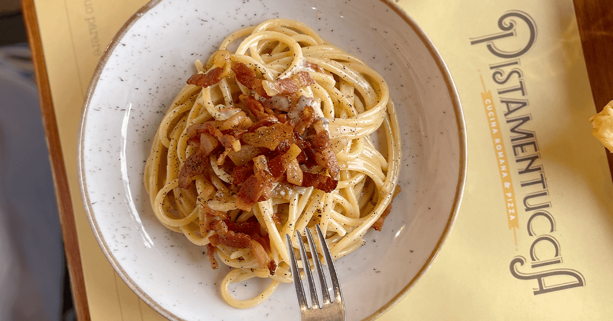 piatto di pasta alla gricia con pecorino e guanciale visto dall'alto con tovaglietta di Pistamentuccia e forchetta a lato